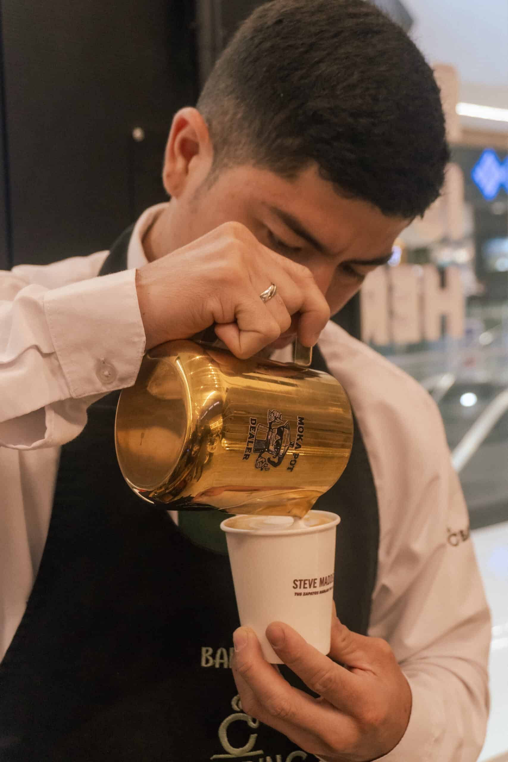Barista pouring latte art with a gold pitcher at an event with coffee catering